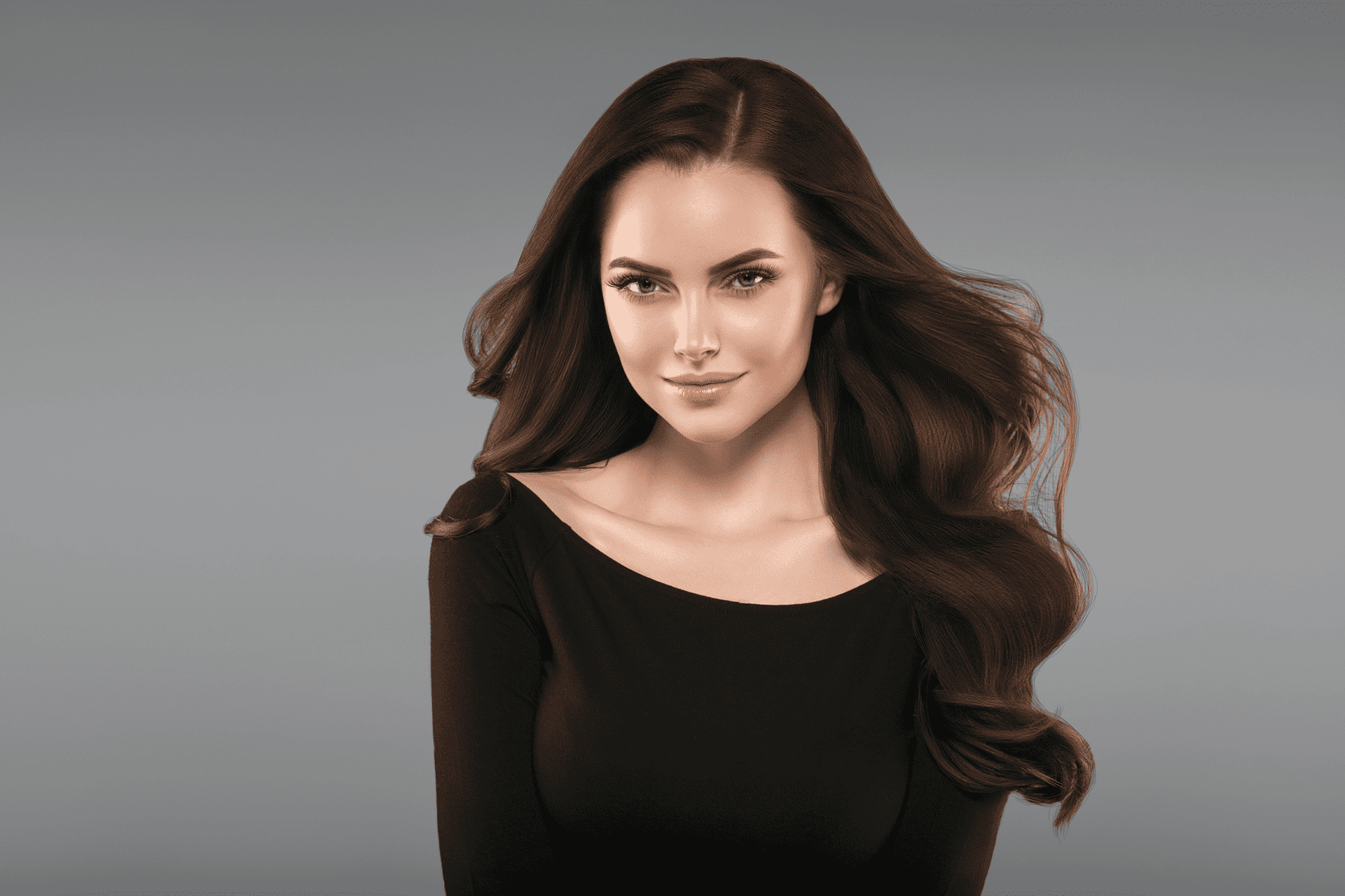 Woman with long brown hair and black top, smiling against a gray background.