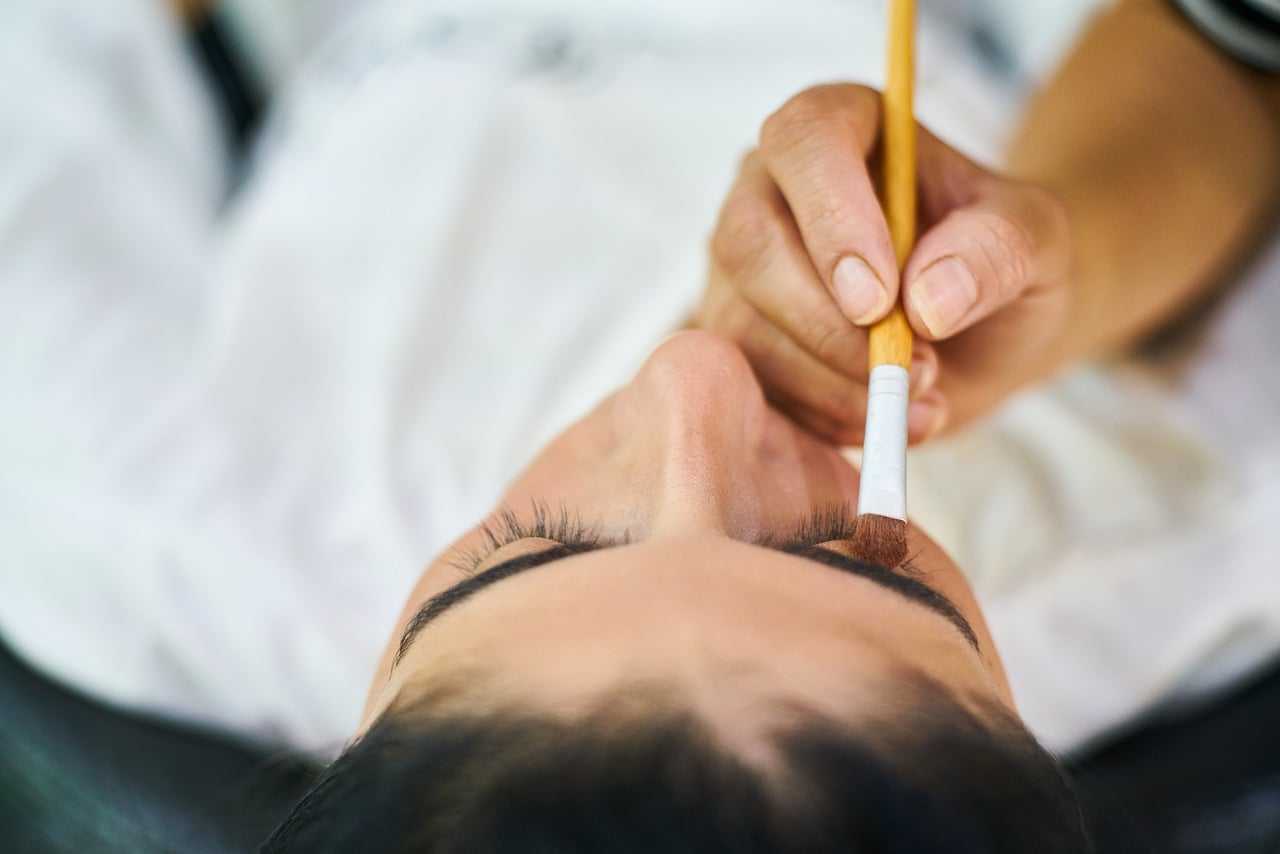 Close-up of a person having their eyeshadow applied with a brush by a makeup artist.
